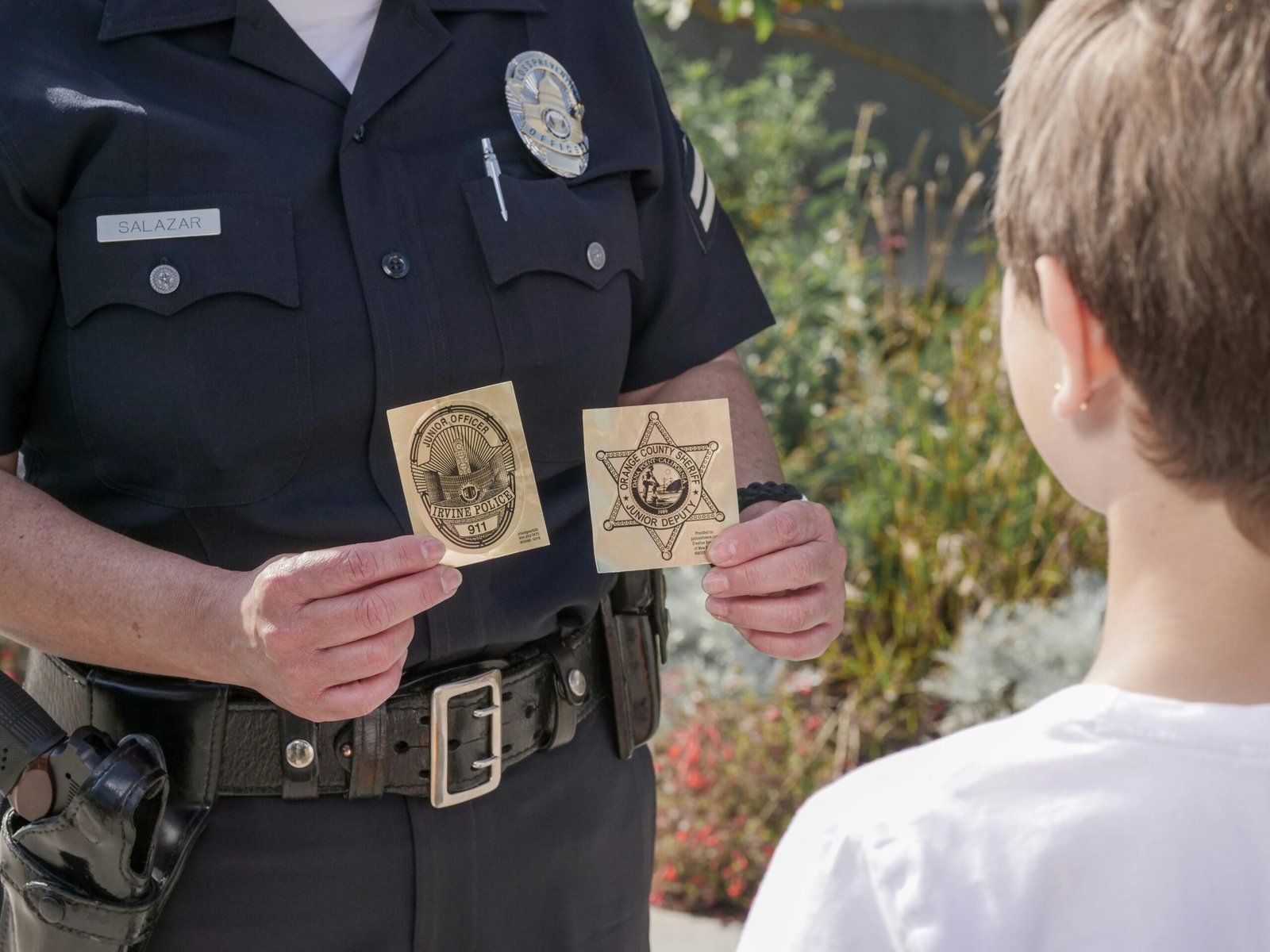 Officer showing law enforcement badges to a child outdoors, fostering positive interaction.